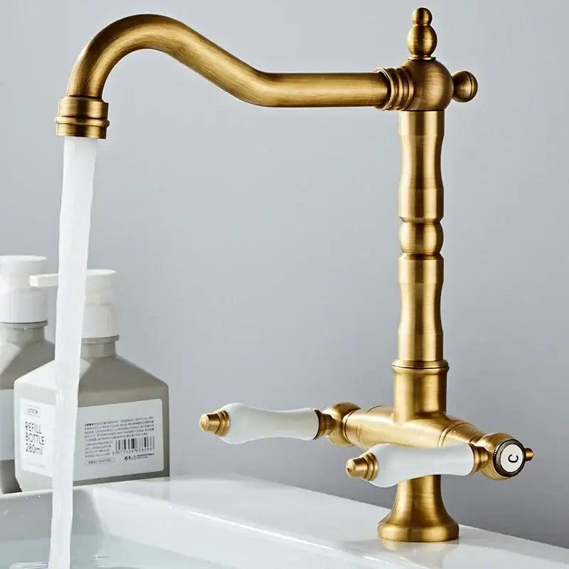 Decorbites antique brass kitchen faucet with dual white ceramic handles, curved spout, ornate base, and 360° rotation