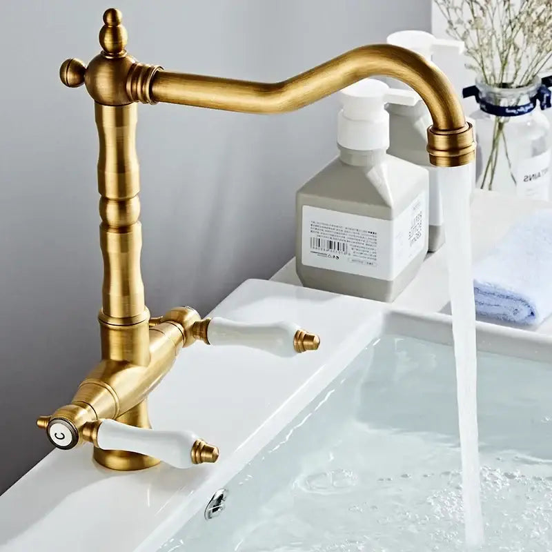 DecorBites antique brass kitchen faucet with dual white ceramic handles, ornate base detailing, and 360° rotation