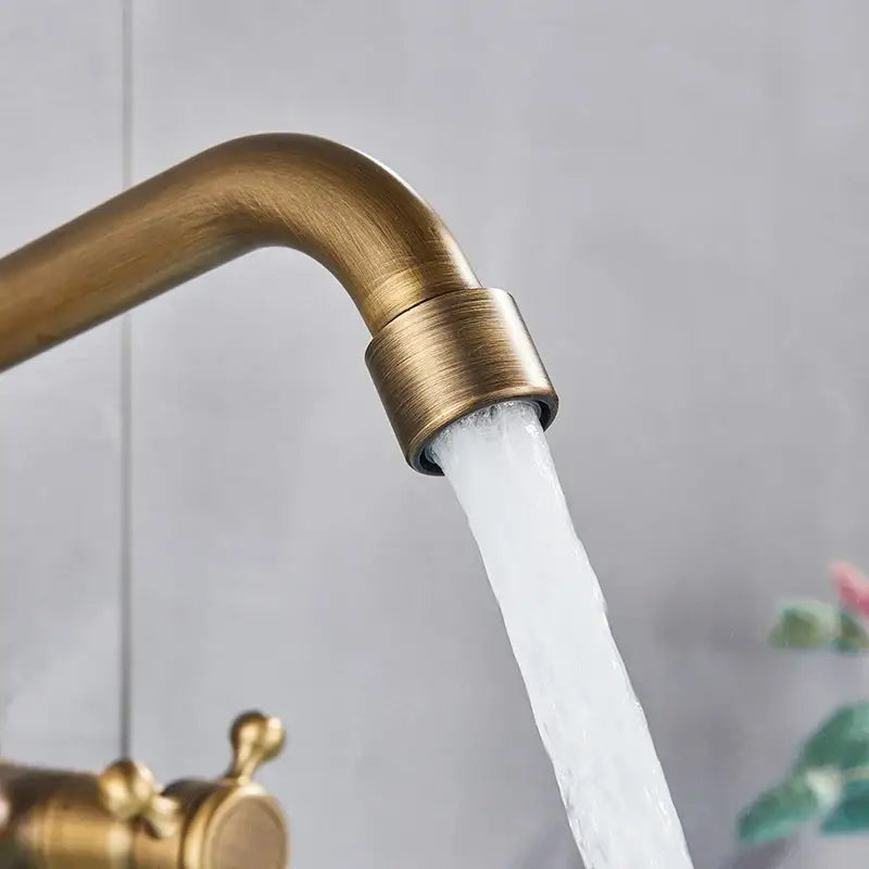 DecorBites™ antique brass kitchen faucet with swivel spout and dual handle mixer flowing water in brass finish