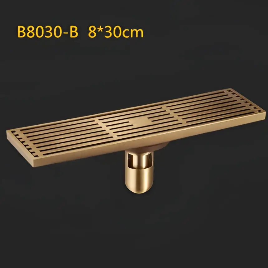 Brass-colored antique brass linear floor drain with slatted art carved cover and cylindrical mounting base for shower use