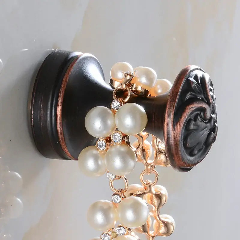 A decorative pearl and crystal necklace with a gold-toned chain displayed near a decorbites™ antique brass robe hook single clothes hanger