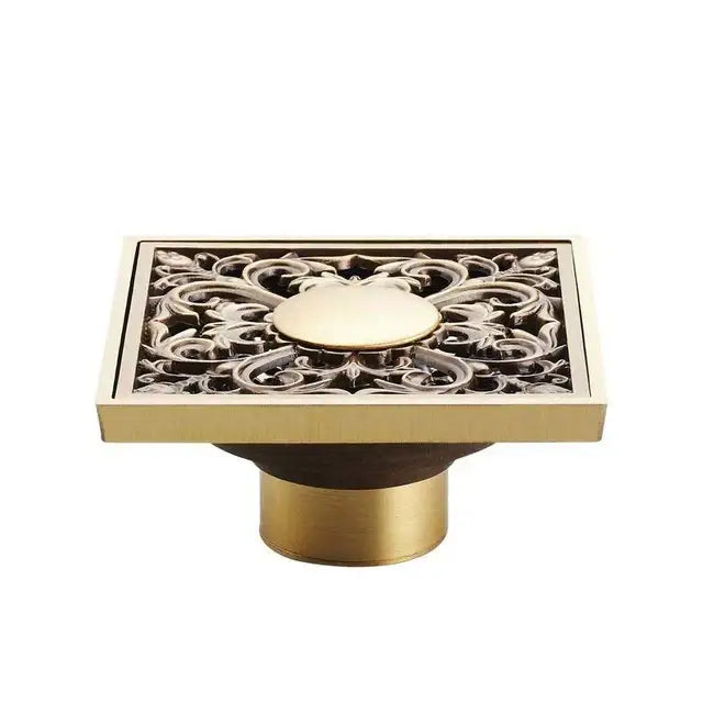 Brass-finished rectangular antique brass shower floor drain with intricate floral cutout and circular medallion design