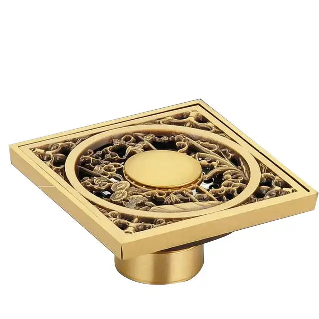 Gold-colored decorbites antique brass shower floor drain with intricate floral and scrollwork design 10cm square grate