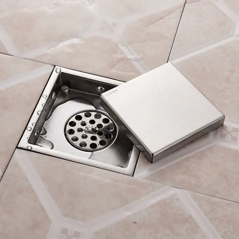 Square stainless steel floor drain with hinged lid and circular grate for antique brass shower drain use by DecorBites