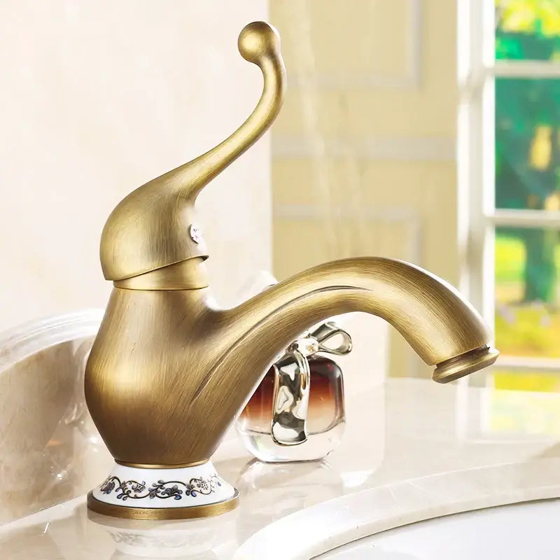 DecorBites antique brass single handle bathroom faucet with ornate curved spout and decorative porcelain base with black floral patterns