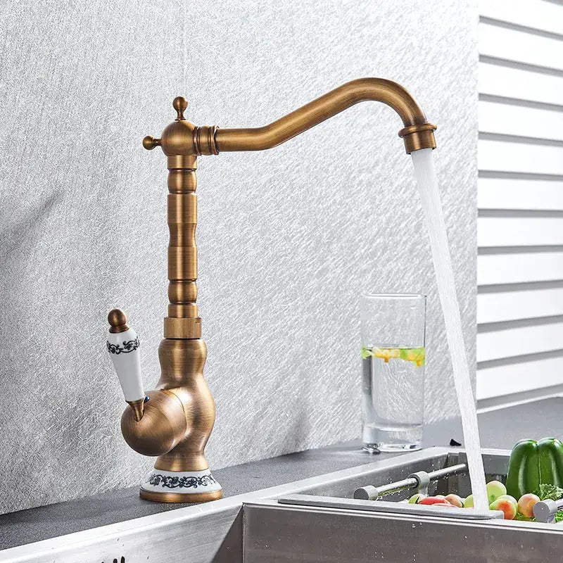 Antique brass kitchen sink faucet with white ceramic handle and black ornate detailing for hot and cold water mixer