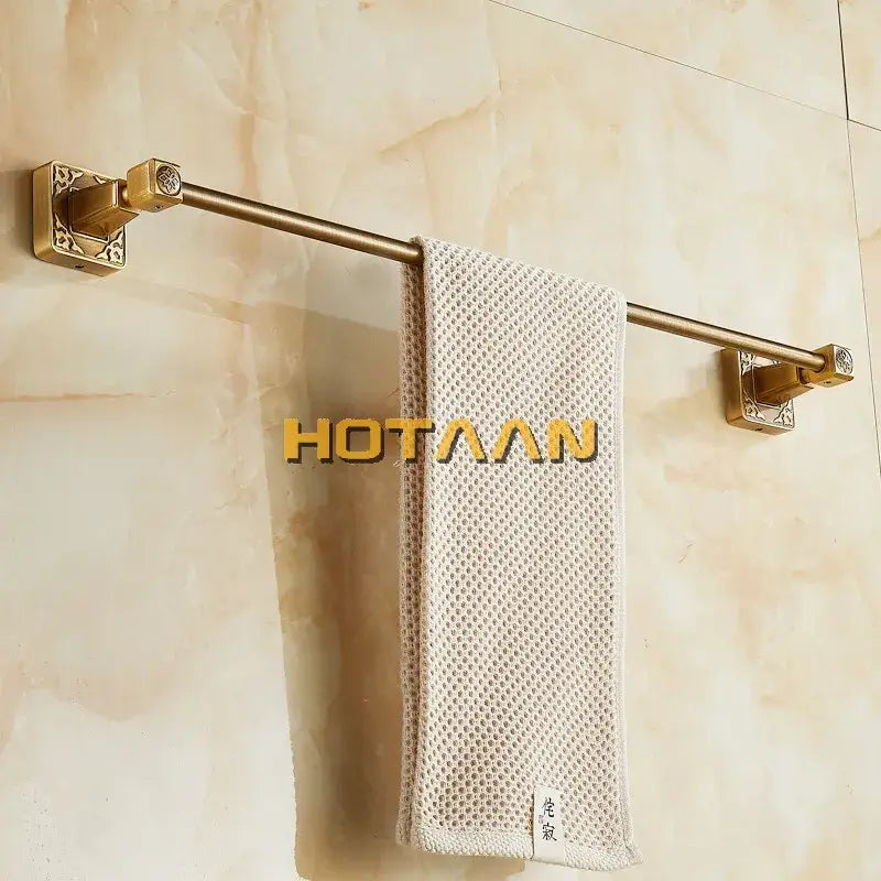 Antique brass single towel bar by DecorBites with ornate square brackets holding a beige textured towel wall mounted