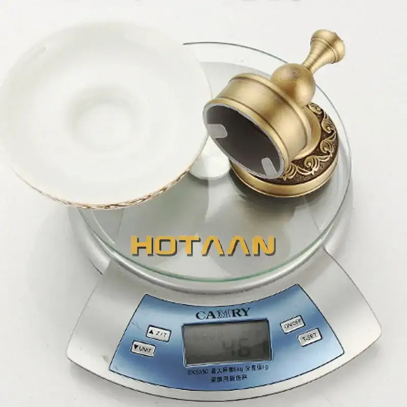 Gold-toned ornate wall-mounted brass soap holder with decorative scrollwork base and cylindrical top for bathroom use