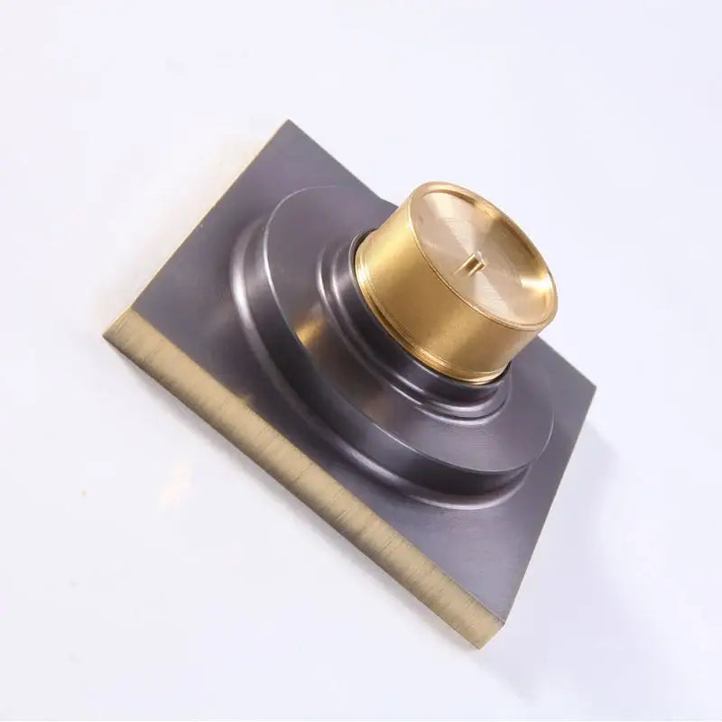 A decorbites antique brass floor drain with a square fish carved design and a brass-finished cylindrical knob top