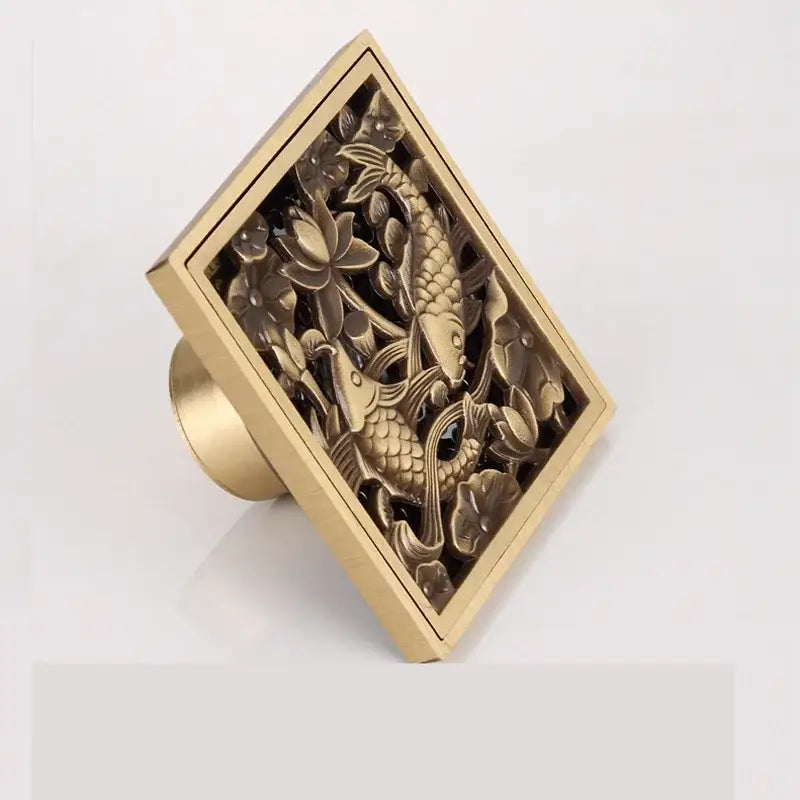DecorBites™ antique brass floor drain features a gold-colored rectangular square fish carved design with lotus flowers