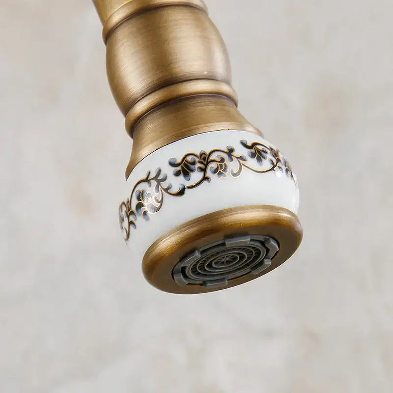 Decorbites antique brass swivel spout kitchen faucet with white ceramic nozzle featuring black and gold floral patterns