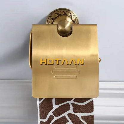 Gold-colored brass toilet paper holder with ornate circular mounting plate and embossed hotaaan branding for bathroom use