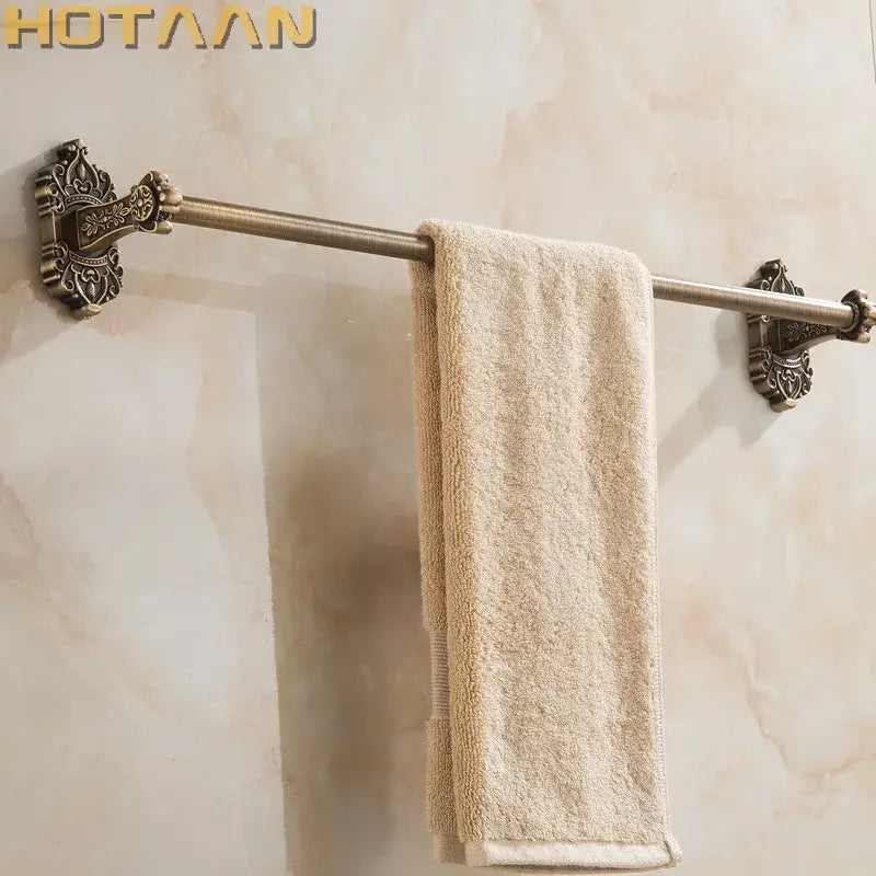 DecorBites™ antique brass towel bar with ornate decorative end plates holding a beige terry cloth towel