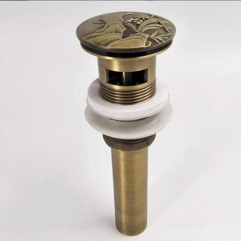 Antique brass vessel sink drain with detailed floral relief top cap and white ceramic washers for bathroom use