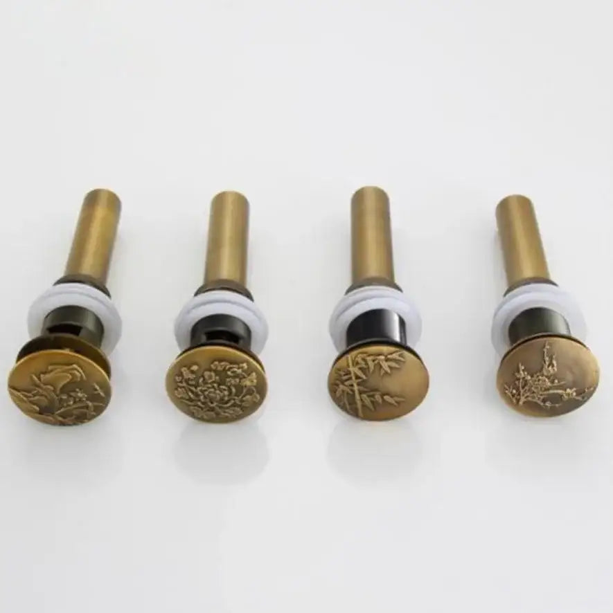 Four brass-finished antique brass vessel sink drain stoppers with engraved floral and bamboo designs for bathroom use