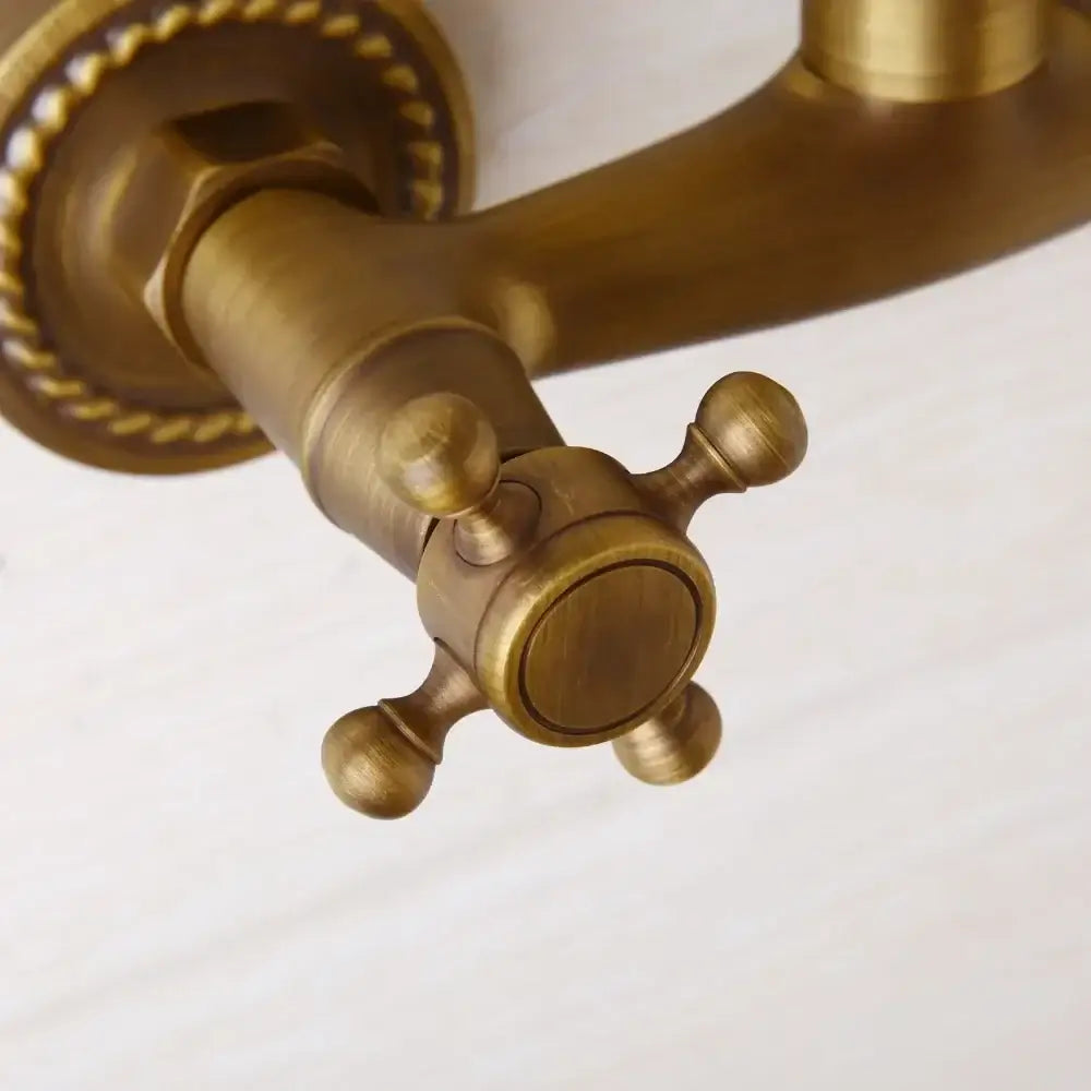 Decorbites antique brass wall mounted shower faucet with antique brass cross-handle and ornate rope detailing on base