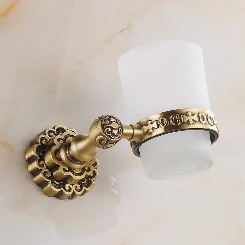 Decorbites antique brass wall mounted toothbrush holder with ornate scrollwork and frosted white cylindrical cup
