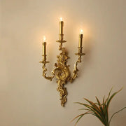 DecorBites™ antique brass wall sconce with three candle-style lights and intricate baroque detailing for elegant lighting