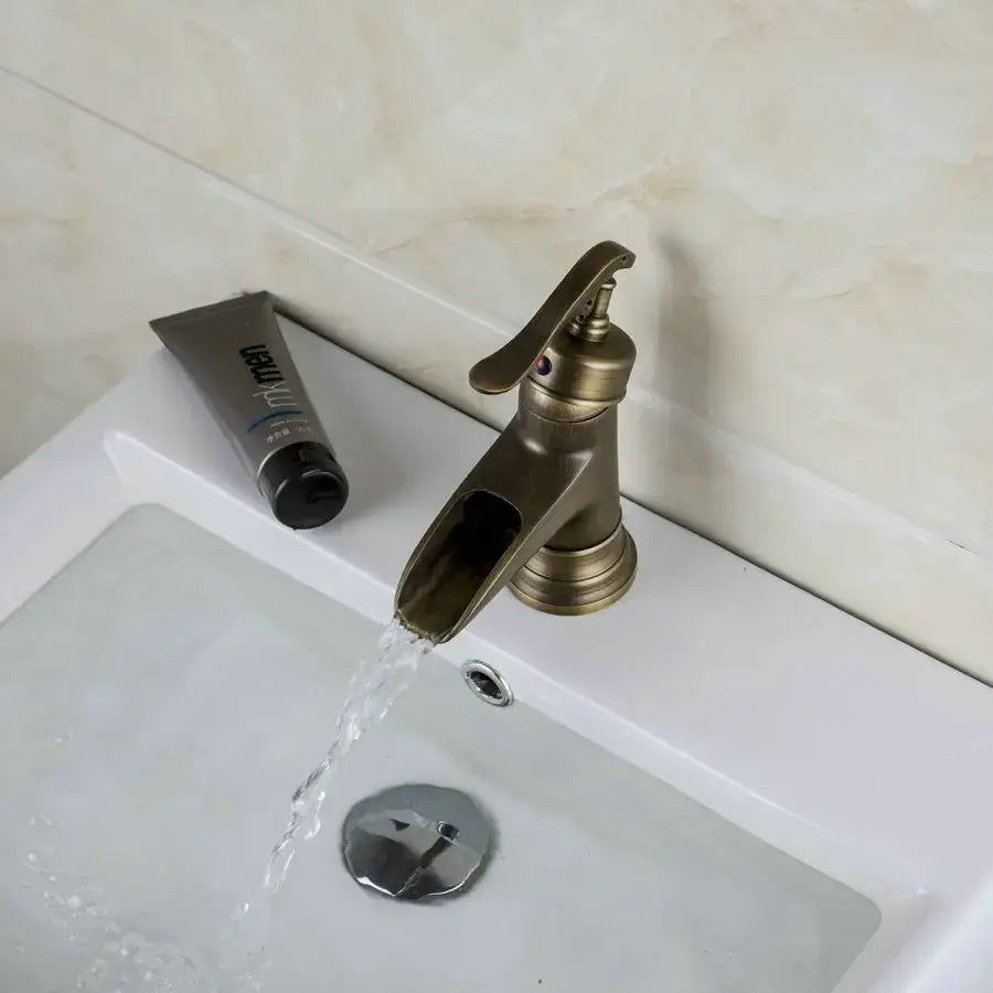 DecorBites antique brass waterfall basin faucet with a sleek curved spout and ornate art design handle