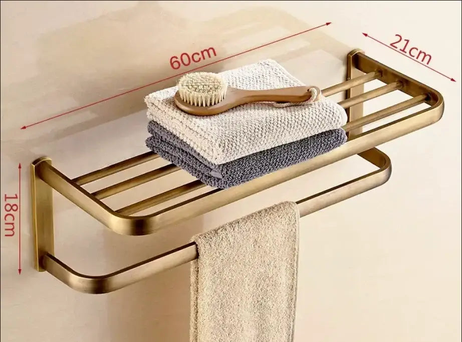 Brass-finished double-tier antique bronze bathroom rack with towel bar shelf holding towels and brush from decorbites