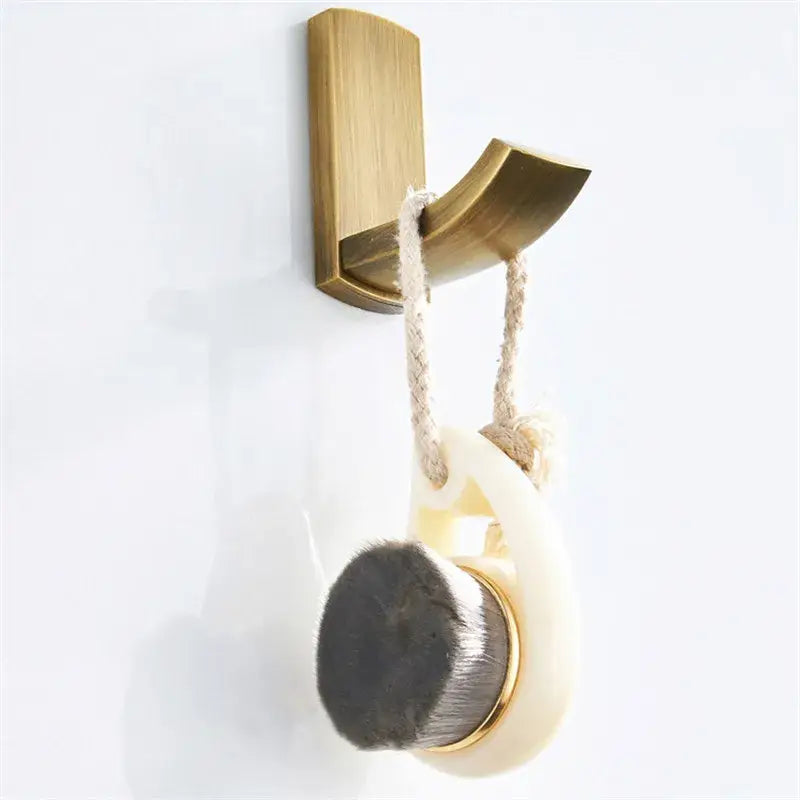 A cream-colored oval bath brush with black bristles and antique bronze metal accents hanging on a brass hook from decorbites antique bronze bathroom accessory set