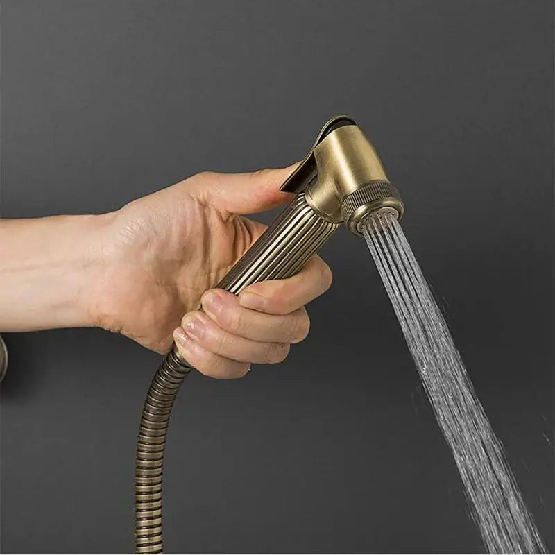 Brass-colored antique bronze douche bidet sprayer with ribbed handle and flexible hose in decorbites™ set with copper valve