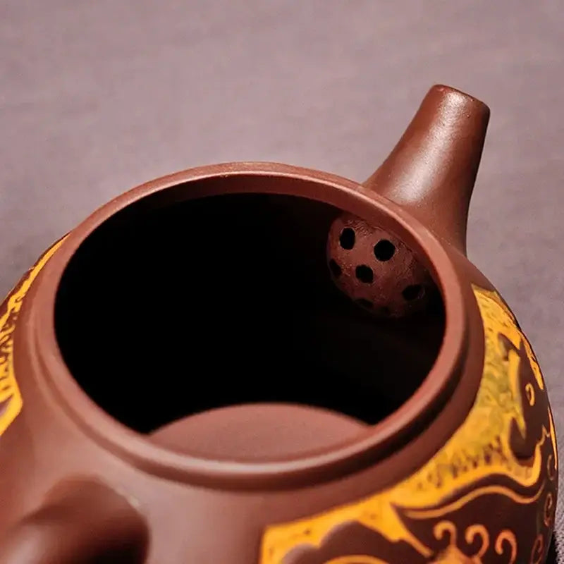 Brown ceramic antique bronze teapot with intricate golden dragon patterns and perforated infuser in bronze teapot set