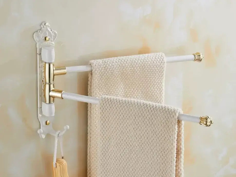 White and gold ornate antique carved swivel towel rack with three bars holding cream textured towels wall mounted