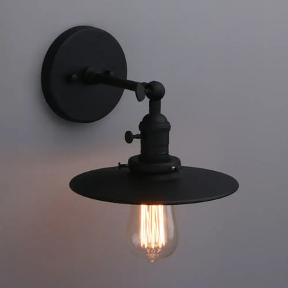 Black industrial wall sconce with antique finish, adjustable arm, wide shade, and clear filament bulb by DecorBites