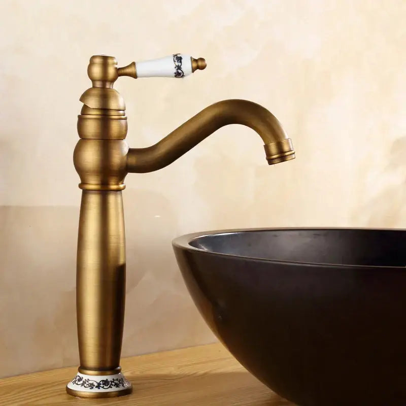 Antique finish brass basin faucet with white ceramic handle featuring black floral detailing and matching decorative base