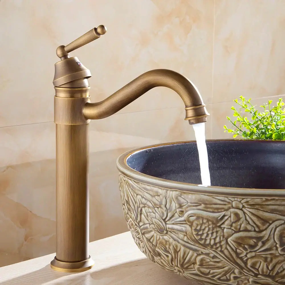 DecorBites™ antique finish brass basin faucet with single handle and curved spout above carved ceramic basin