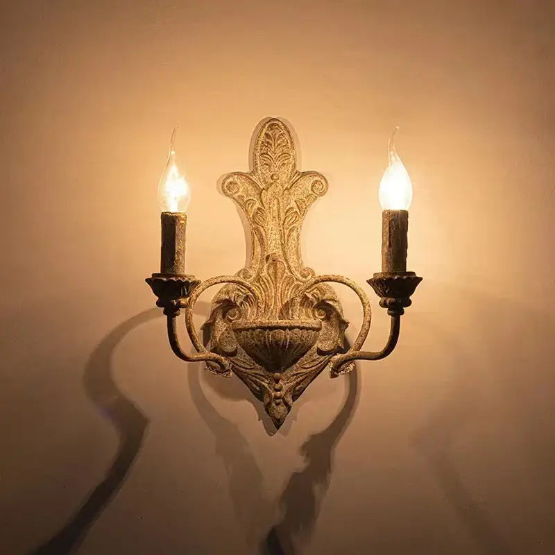Antique iron double headed wall lamp by DecorBites featuring brass ornate leaf scrollwork with two lit candle bulbs