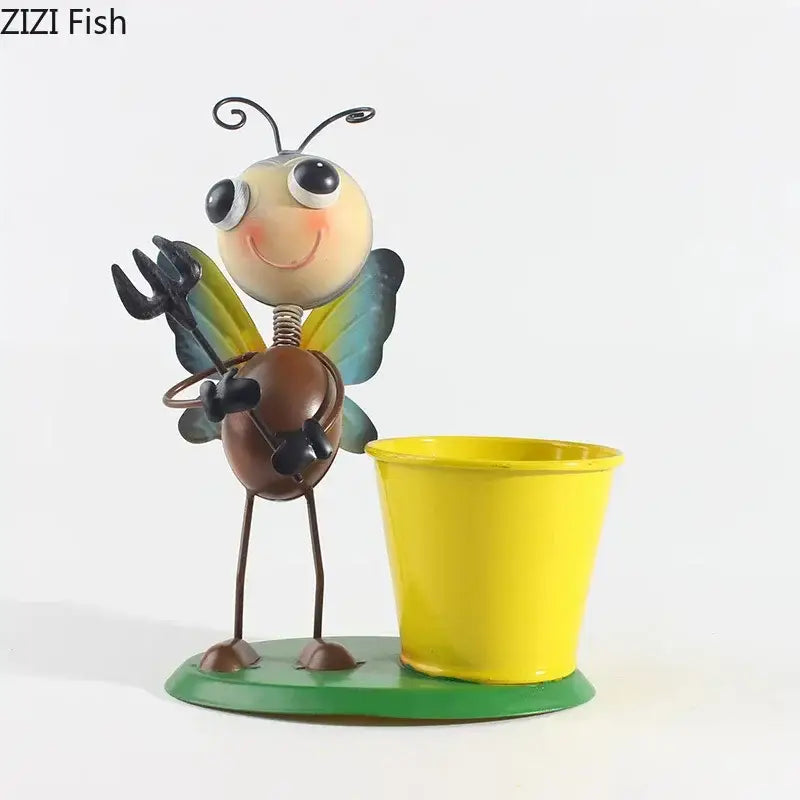 A whimsical metal bee figurine with yellow and blue wings stands beside a bright yellow pot in the decorbites ants gardener vase