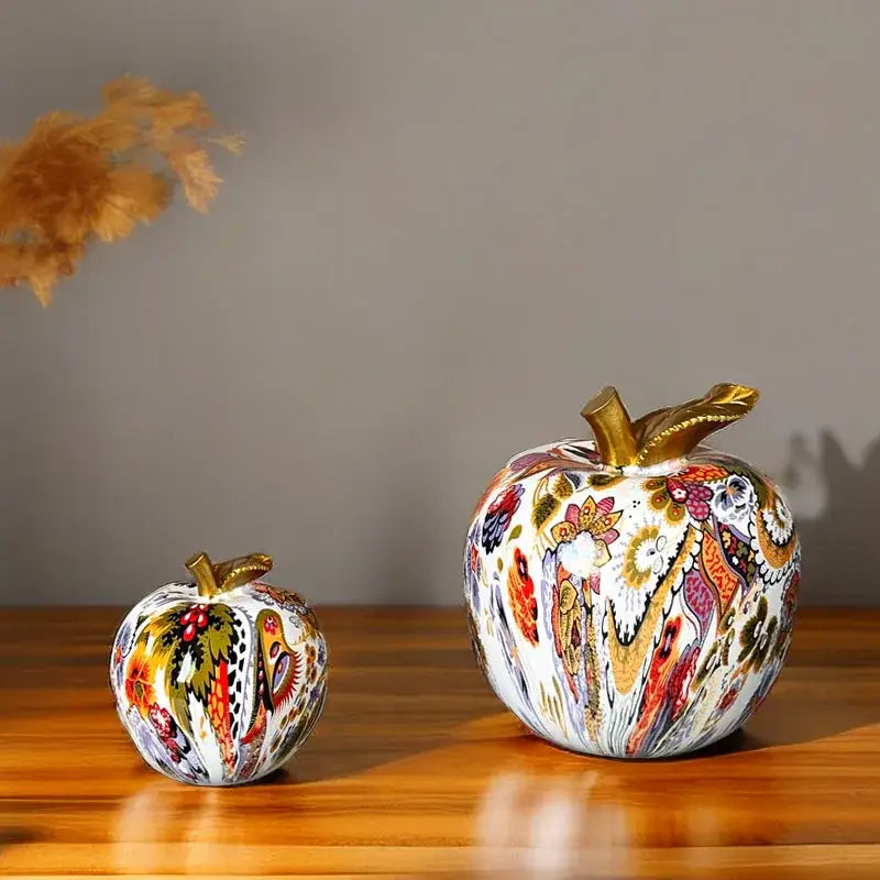 Two intricately painted decorbites apple resin figures with gold stems featuring floral and paisley patterns on white base