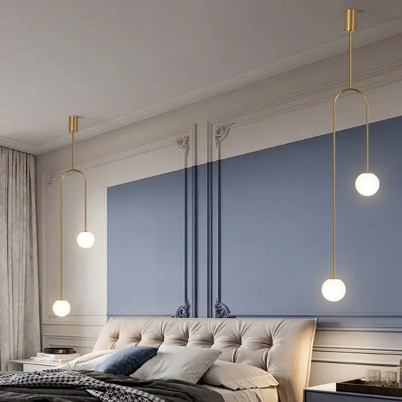 Three gold-toned spherical glass decorbites arc line chandelier pendant lights hanging above tufted bed