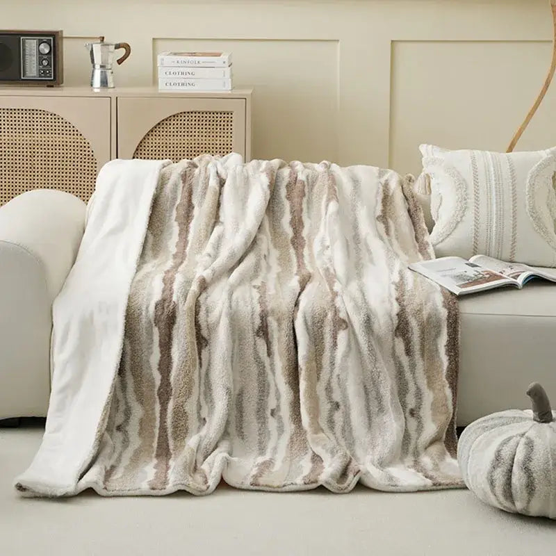 A plush decorbites arctic velvet faux rabbit throw blanket in cream and taupe stripes draped over a sofa