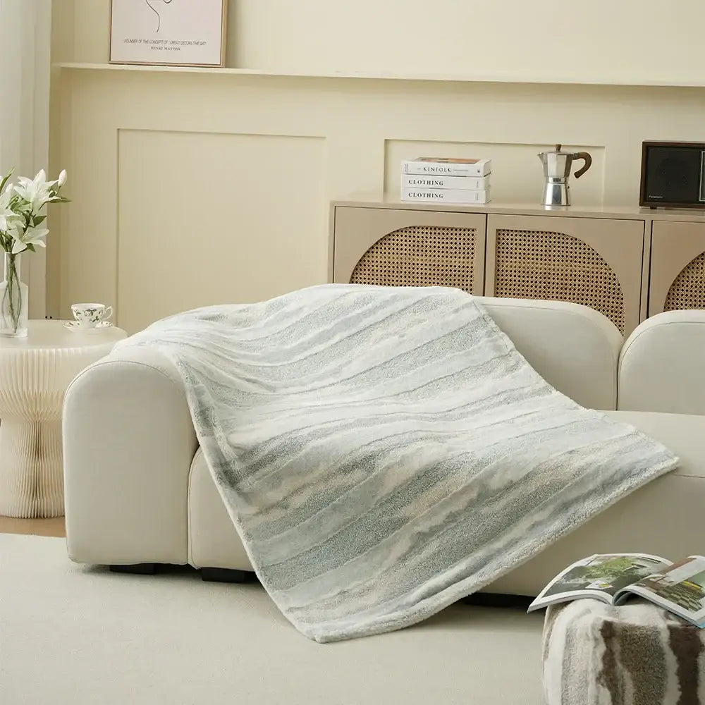 A soft light gray decorbites arctic velvet faux rabbit throw blanket with subtle texture draped over a modern sofa
