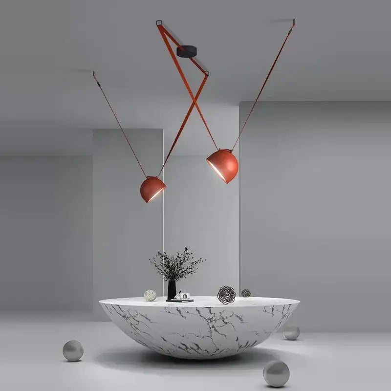 Modern copper-toned cross belt hanging lamp with orange lustre and articulated arms above white marble table