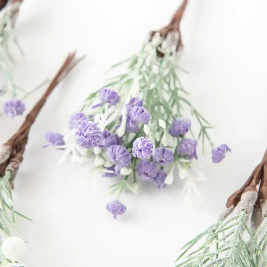 A delicate cluster of artificial gypsophila plants with soft purple blooms and pale green stems on rustic brown twig