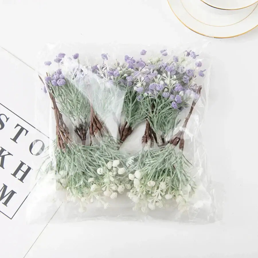 A clear plastic bag containing decorbites artificial gypsophila plants with lavender and white blossoms set of 12