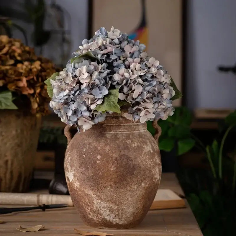 A rustic ceramic vase with decorbites artificial hydrangea silk flower arrangement in soft blue and white hues