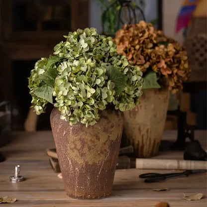 A rustic brown ceramic vase holding a lush green decorbites artificial hydrangea silk flower arrangement for wedding decor