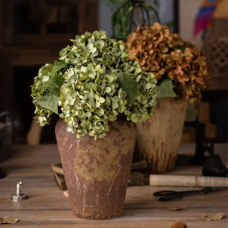 A rustic brown ceramic vase holding a lush green decorbites artificial hydrangea silk flower arrangement for wedding decor