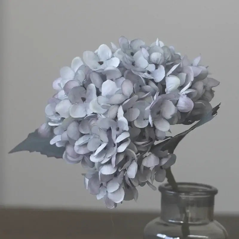 A delicate cluster of pale blue decorbites artificial hydrangea silk flowers in a clear glass vase for wedding decor