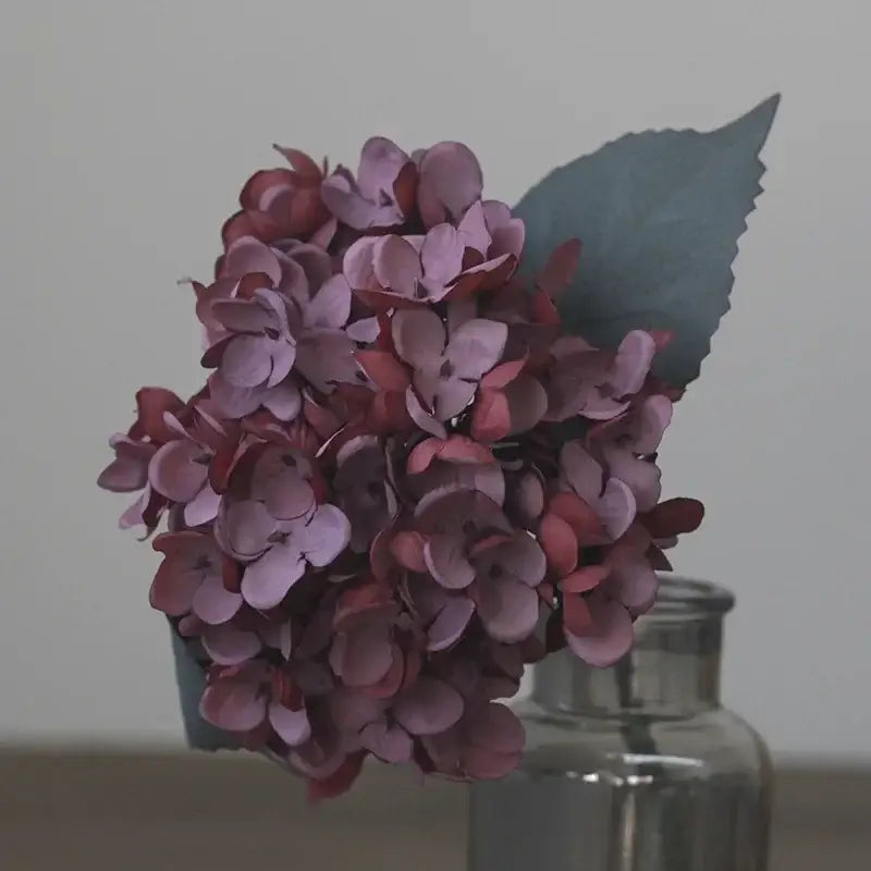 A cluster of decorbites artificial hydrangea silk flowers in soft purple and deep rose with a dark green leaf
