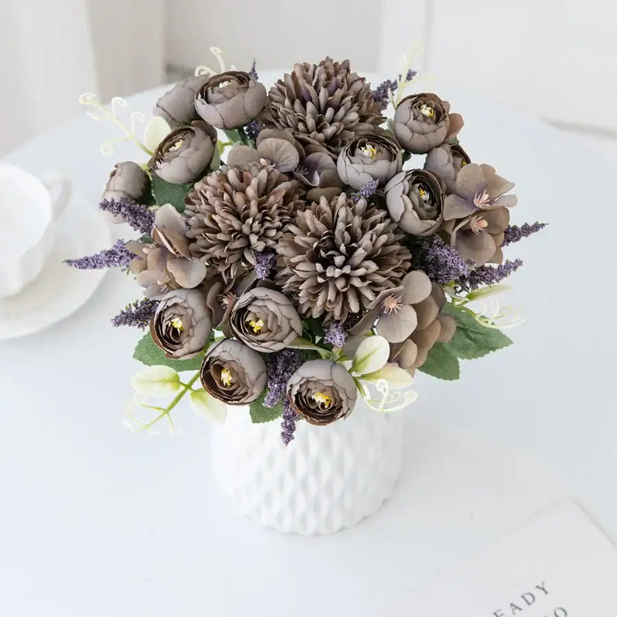 A textured white ceramic vase holding a decorbites artificial hydrangea tea rose bouquet in muted tones with green leaves