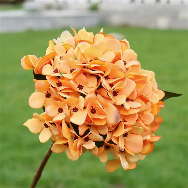 A vibrant orange artificial hydrangea wedding bouquet with delicate layered petals and dark brown centers for indoor decor