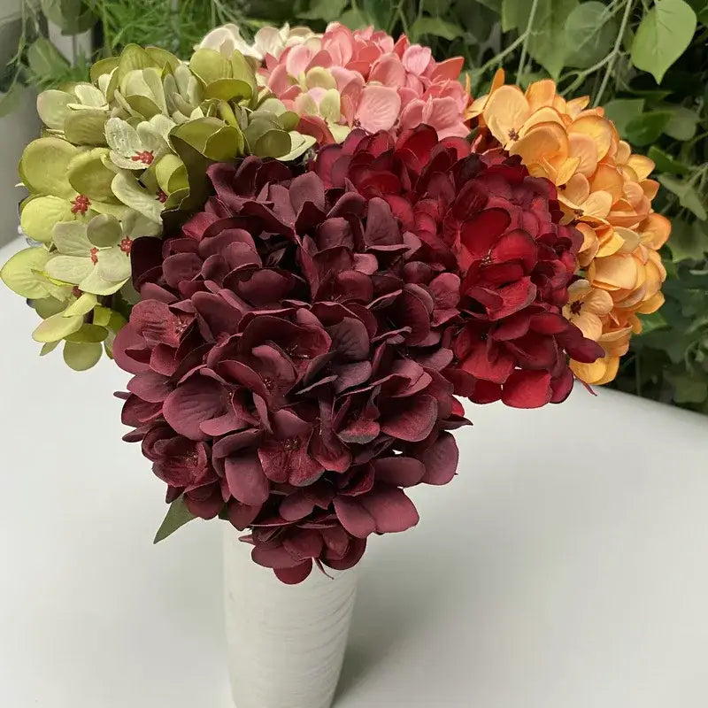 A vibrant artificial hydrangea wedding bouquet in burgundy pink and yellow in a white ceramic vase for indoor decor