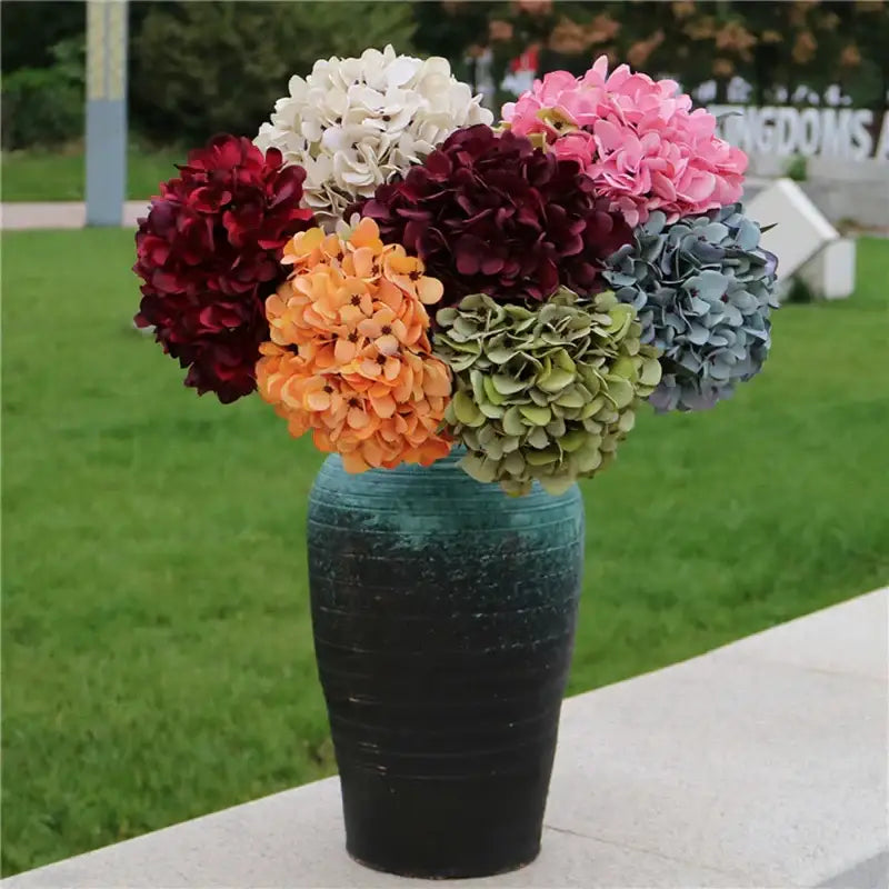 A vibrant artificial hydrangea wedding bouquet in multicolor shades arranged in a teal-to-black ceramic vase for indoor decor