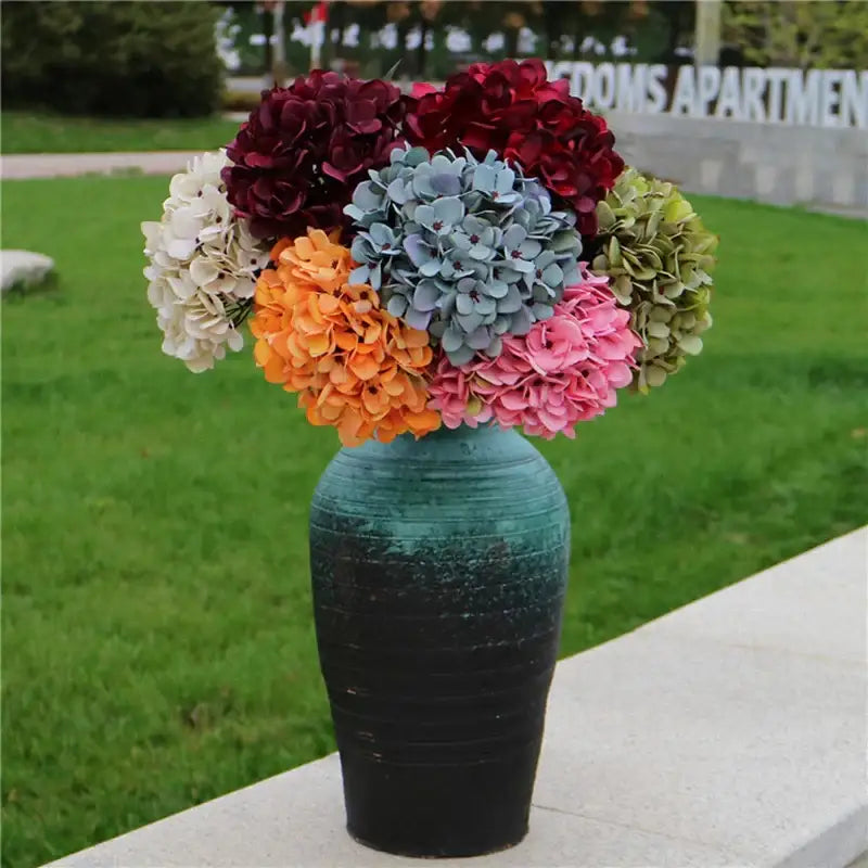 A vibrant artificial hydrangea wedding bouquet in maroon white blue orange pink and green in a teal black ceramic vase
